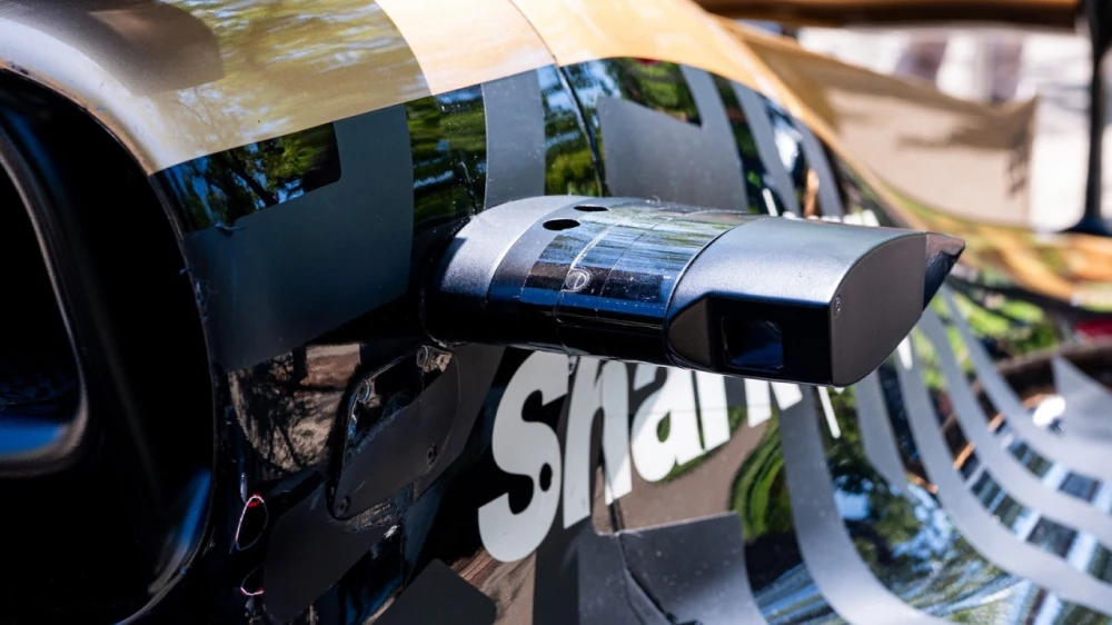 A cinematographer holds an innovative iPhone shooting rig, filming a scene on the racetrack
