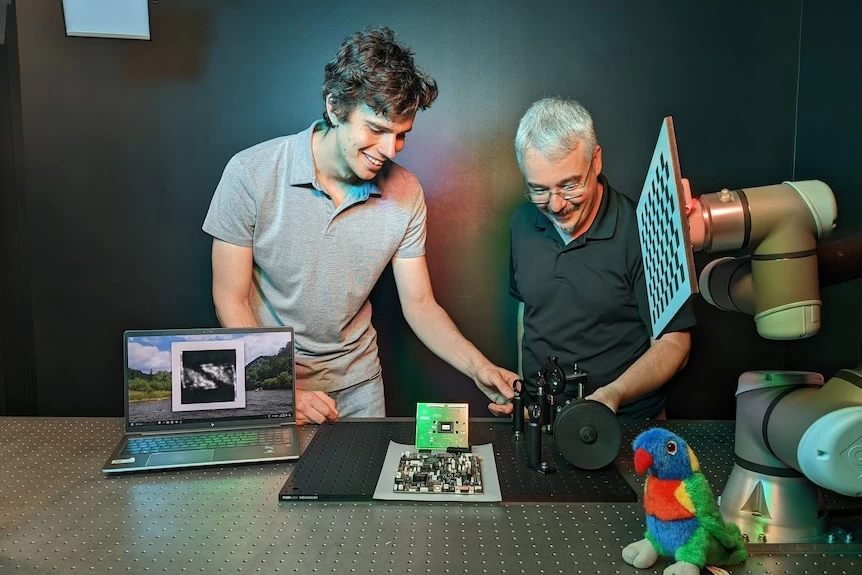 Two men stand behind a camera attached to a board.